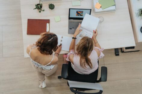 Two women with notepads and a laptop